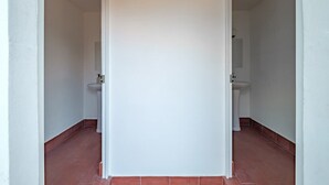 A narrow hallway with white walls and red-tiled flooring, leading to a bathroom with a sink and toilet. - CAM 1-Bedroom Deluxe (Ciudad de México)
