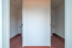 A narrow hallway with white walls and red-tiled flooring, leading to a bathroom with a sink and toilet. - CAM 1-Bedroom Deluxe (Ciudad de México)