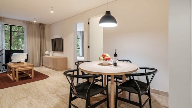 A modern dining area with a round table, black chairs, a pendant light, and a view of the outdoors through large windows. - CAM 1-Bedroom Deluxe (Ciudad de México)