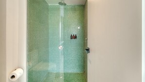 Eine Dusche mit Glastür und grünen Mosaikfliesen.