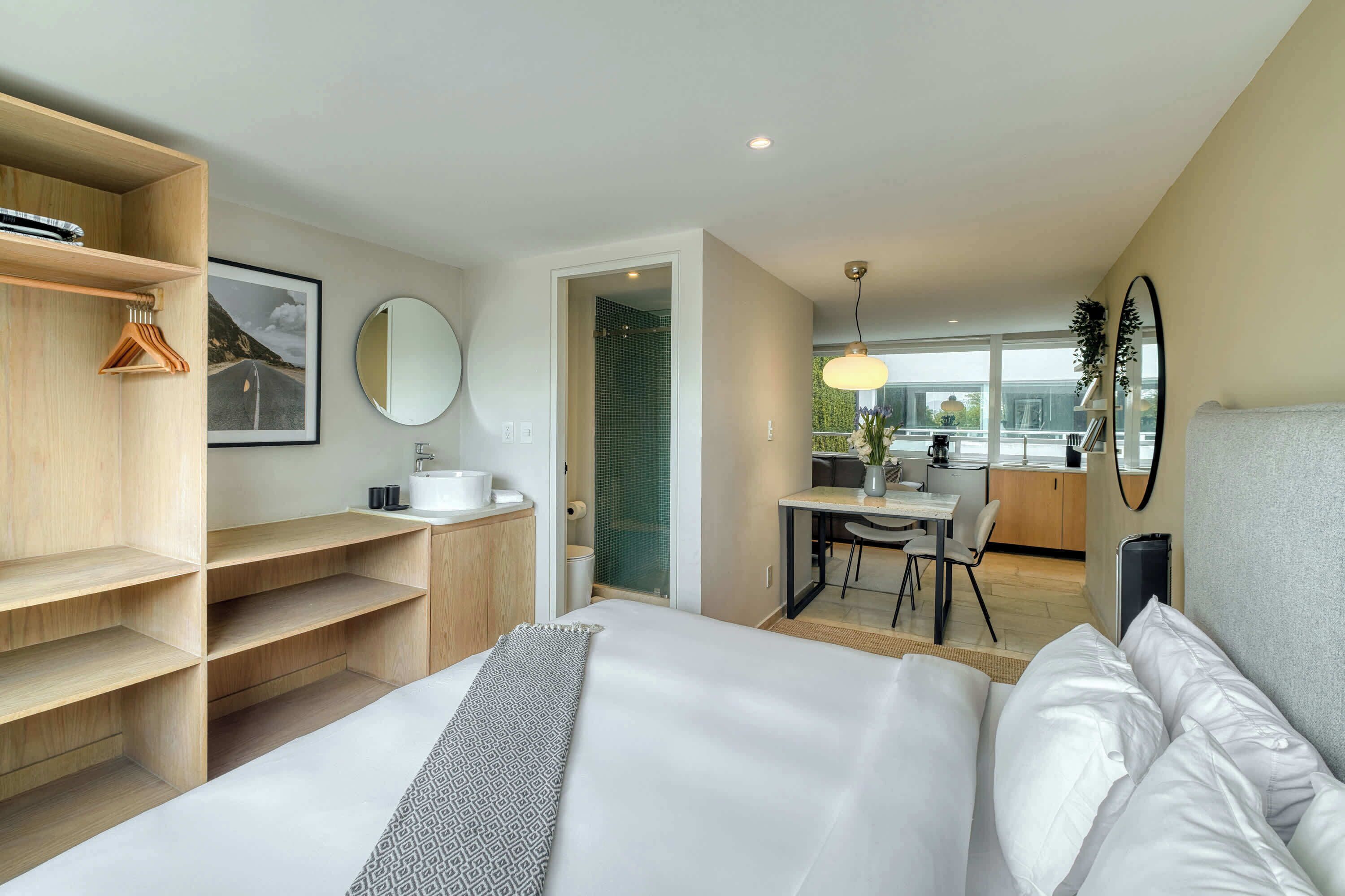 A modern hotel room with a bed, a wooden wardrobe, a bathroom, and a dining area.