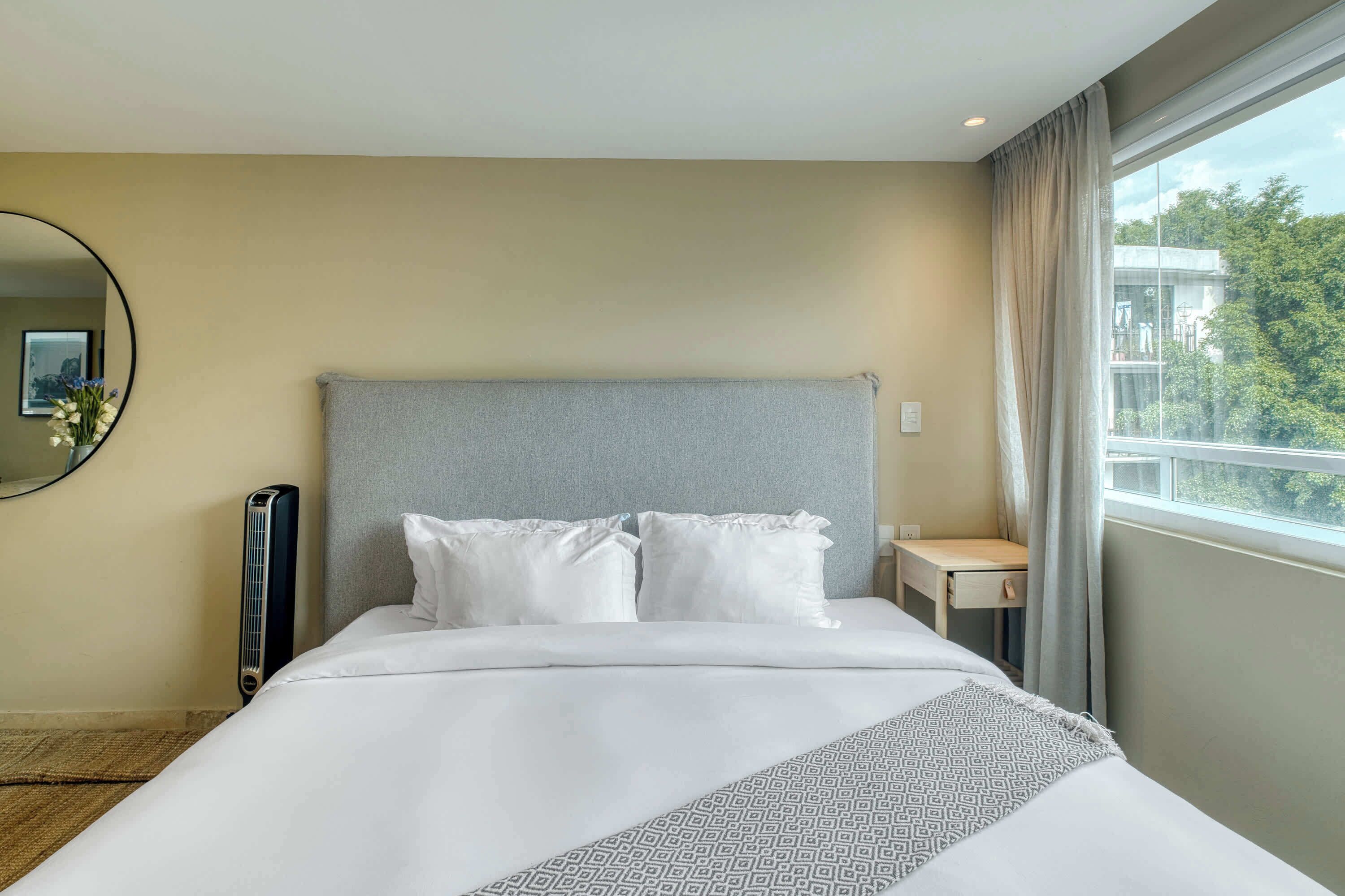 Une chambre d’hôtel avec un lit, une table de chevet, un miroir et une fenêtre avec des rideaux.