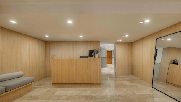 A modern reception area with a wooden reception desk, a grey sofa, and a large mirror. - Modern King Studio in Central Roma Norte (Ciudad de México)