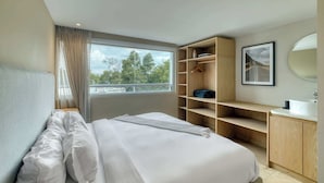 A bedroom with a bed, a window with curtains, a wooden wardrobe, a mirror, and a framed picture on the wall. - Modern King Studio in Central Roma Norte (Ciudad de México)