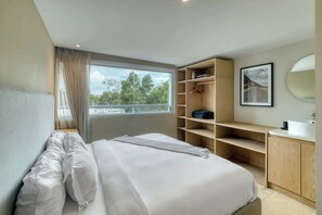 Ein Schlafzimmer mit einem Bett, einem Fenster mit Vorhängen, einem Holzschrank, einem Spiegel und einem gerahmten Bild an der Wand.