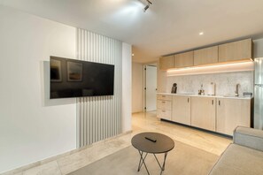 A modern kitchen with a flat-screen TV, wooden cabinets, and a small round table. - Modern King Studio in Central Roma Norte (Ciudad de México)