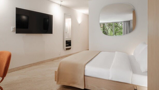 Habitación de hotel moderna con cama, televisión montada en la pared, espejo y vista a zonas verdes.