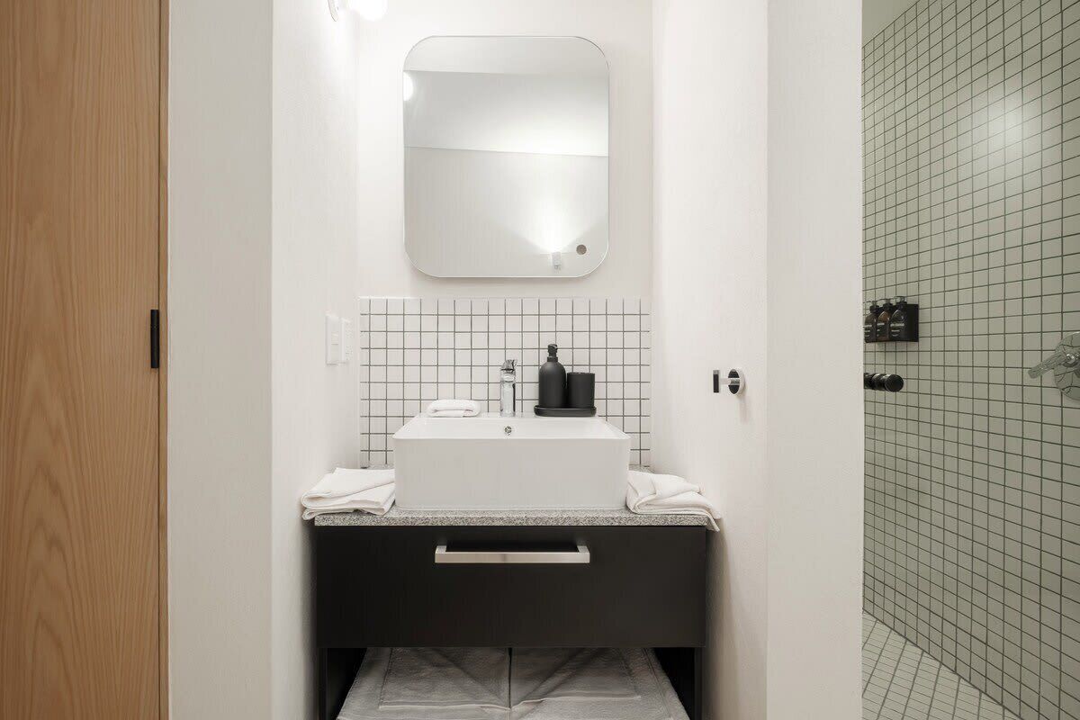 Een badkamer met een witte wastafel, een spiegel en een betegelde douchewand.