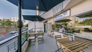 An outdoor seating area with tables and chairs, a sign for "The Blue Cup Coffee & Waffles", and a view of the street and buildings in the background. - Flat in Regatta Ii with breakfast included 204 (Santo Domingo)