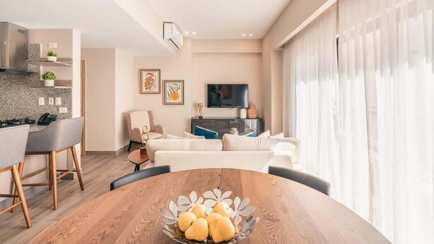 Ein modernes Wohnzimmer mit einem Holzesstisch, einer Couch und einem Fernseher im Hintergrund.