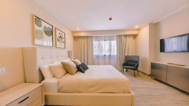 A hotel room with a large bed, a TV mounted on the wall, a desk with a lamp, and a chair. - Regatta Living Ii with Breakfast Included! - 905 (Santo Domingo)