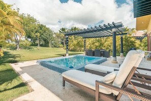 Ein Schwimmbad mit Liegestühlen, einer Pergola und einem gepflegten Rasen.
