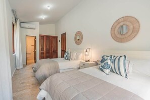 Ein Hotelzimmer mit zwei Betten, einem Nachttisch mit Lampe, einem Spiegel und einer Tür zu einem weiteren Raum.