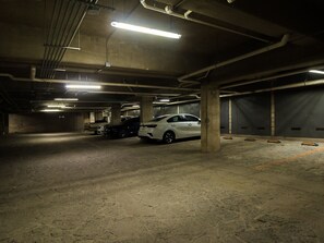 Een ondergrondse parkeergarage met betonnen pilaren, neonverlichting en een witte auto in het midden.