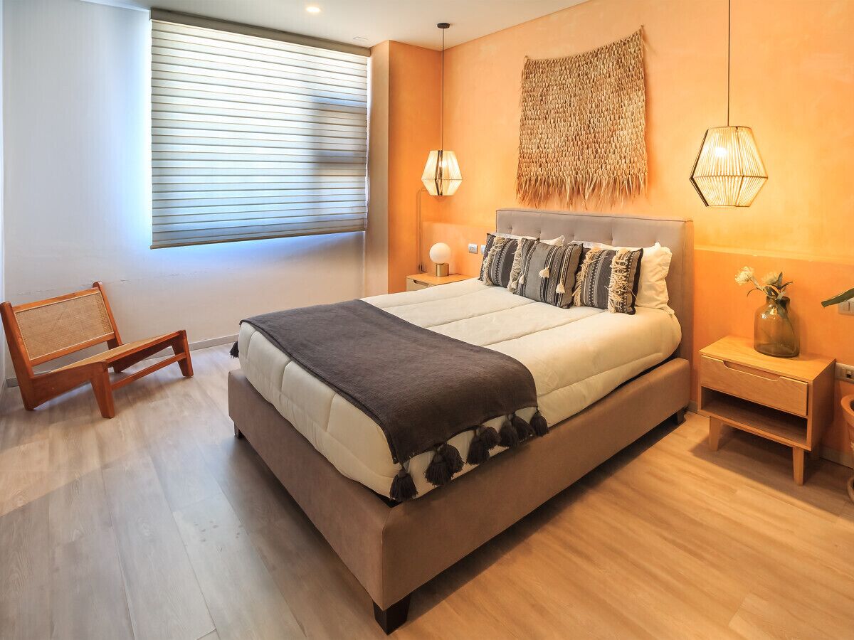A modern bedroom with a large bed, a bedside table, a lamp, and a chair.