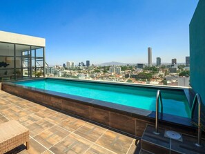 Ein Dachpool mit Blick auf die Stadt, ein wintergartenartiger Raum und eine geflieste Terrasse.
