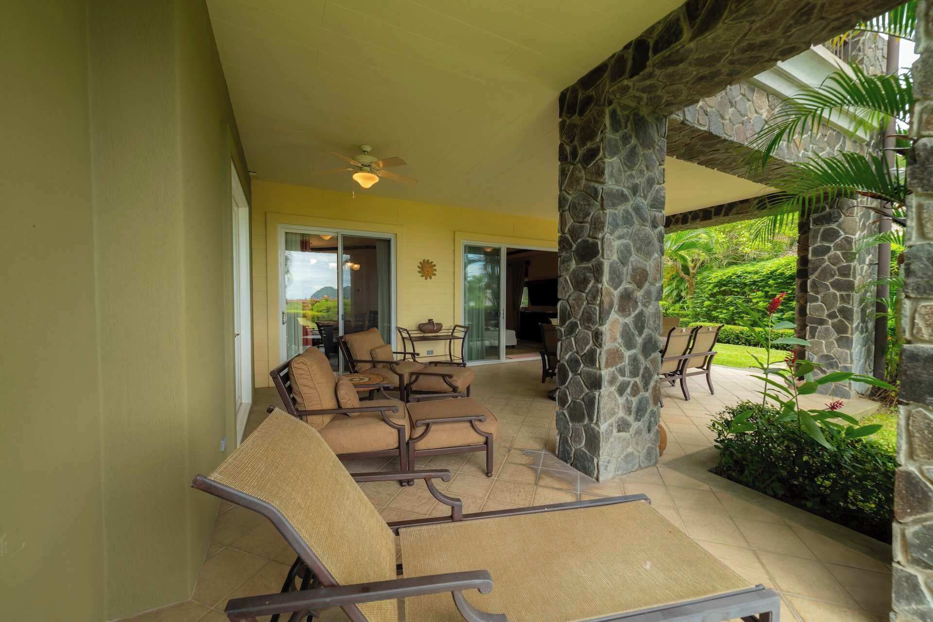Un espace extérieur abrité, aménagé avec des chaises et une table, des piliers en pierre et offrant une vue sur un jardin luxuriant.