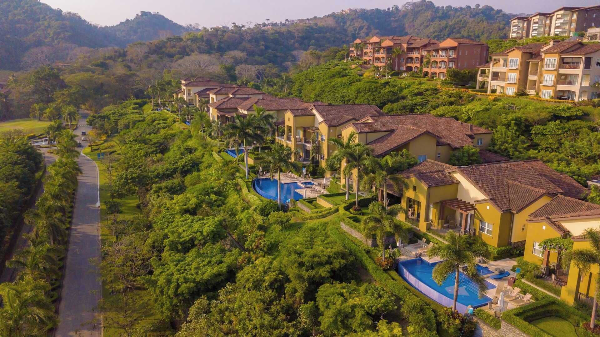 A residential area with multiple two-story houses, a swimming pool, and lush greenery.