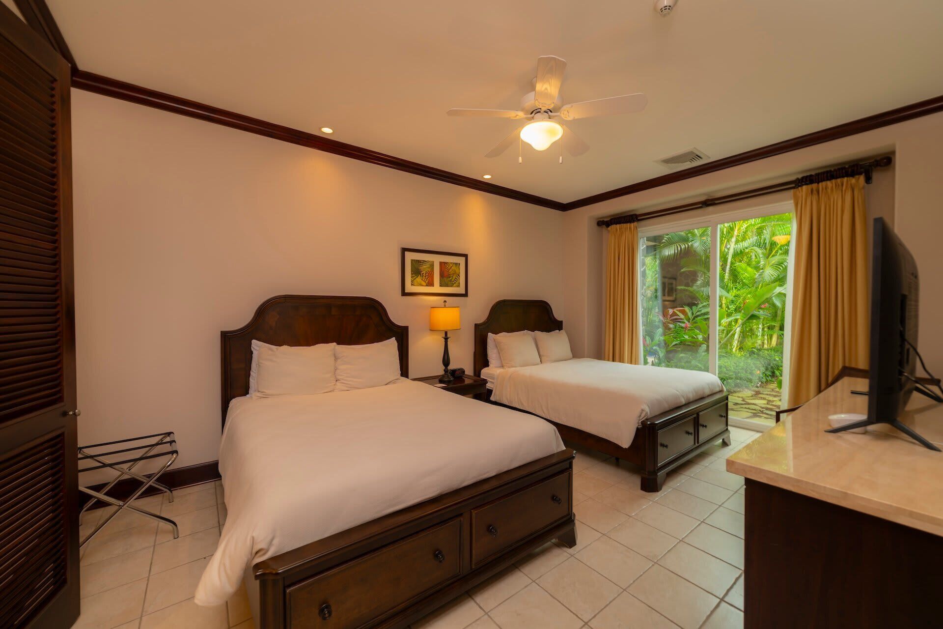A hotel room with two beds, a ceiling fan, a desk, and a window with curtains.