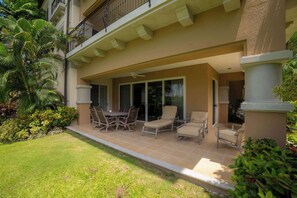 Eine überdachte Terrasse mit Esstisch und Stühlen, eine Sitzecke mit einer Couch und Blick auf ein Gebäude mit Balkon.