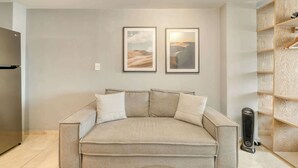A neutral-toned living room with a sofa, two framed pictures on the wall, a built-in wooden shelving unit, and a standing heater. - Modern King Studio in Central Roma Norte (Ciudad de México)