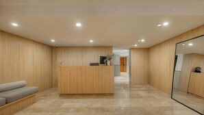 A modern reception area with a wooden reception desk, a grey sofa, and a large mirror. - Modern King Studio in Central Roma Norte (Ciudad de México)