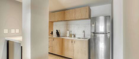 A modern kitchen with wooden cabinets, a stainless steel refrigerator, and a white countertop.