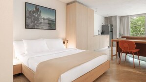Habitación de hotel con cama, escritorio, silla, refrigerador y ventana con vista.