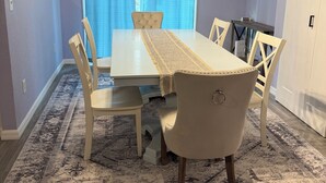 Et spiseområde med et bord, stole, et mønstret tæppe og et vindue med gardiner.