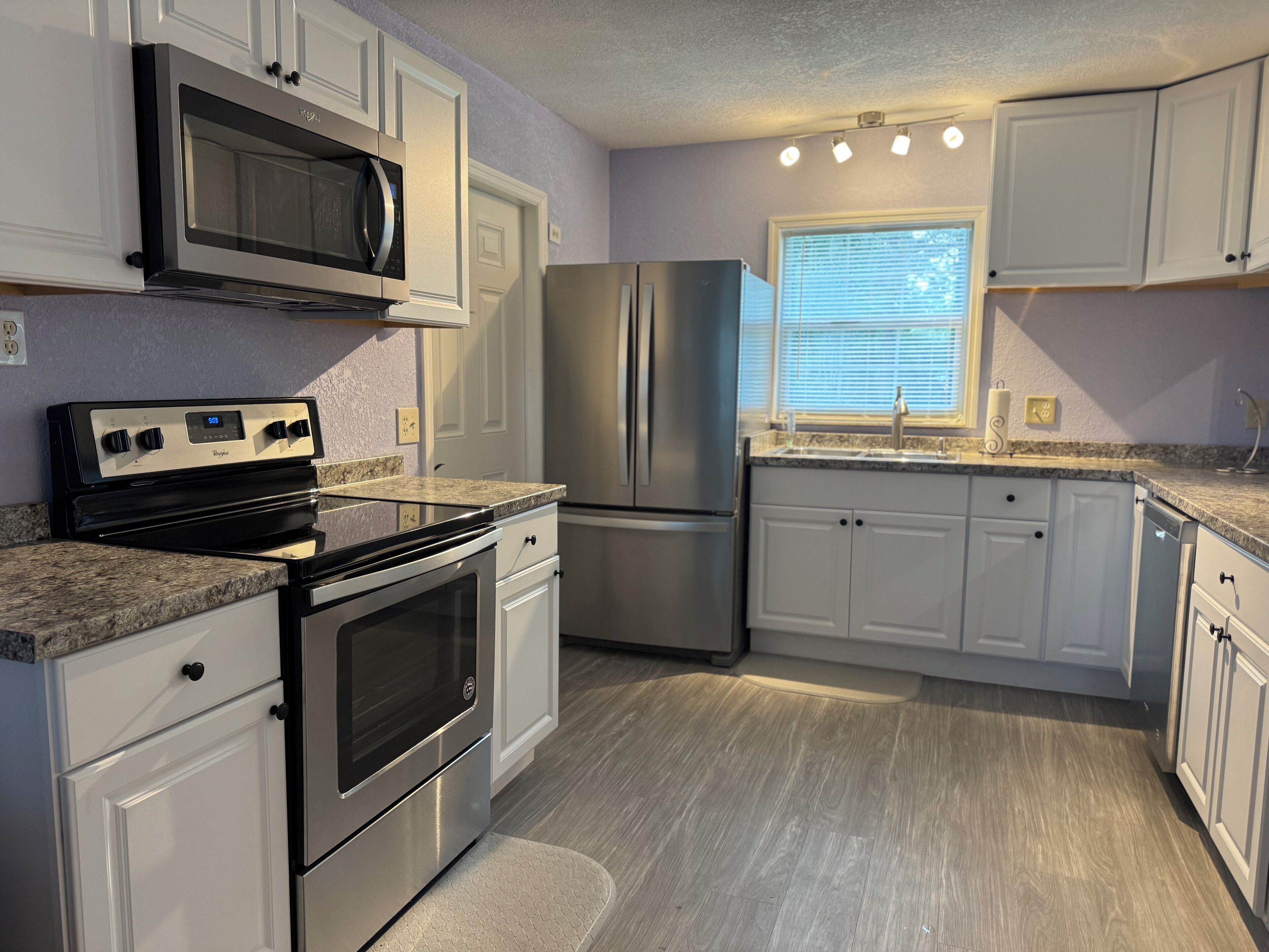 A modern kitchen with stainless steel appliances, white cabinetry, and a granite countertop.