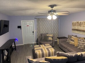 Ein Wohnzimmer mit Deckenventilator, einer Couch, einem Couchtisch, einem Fernseher und gemusterten Vorhängen.