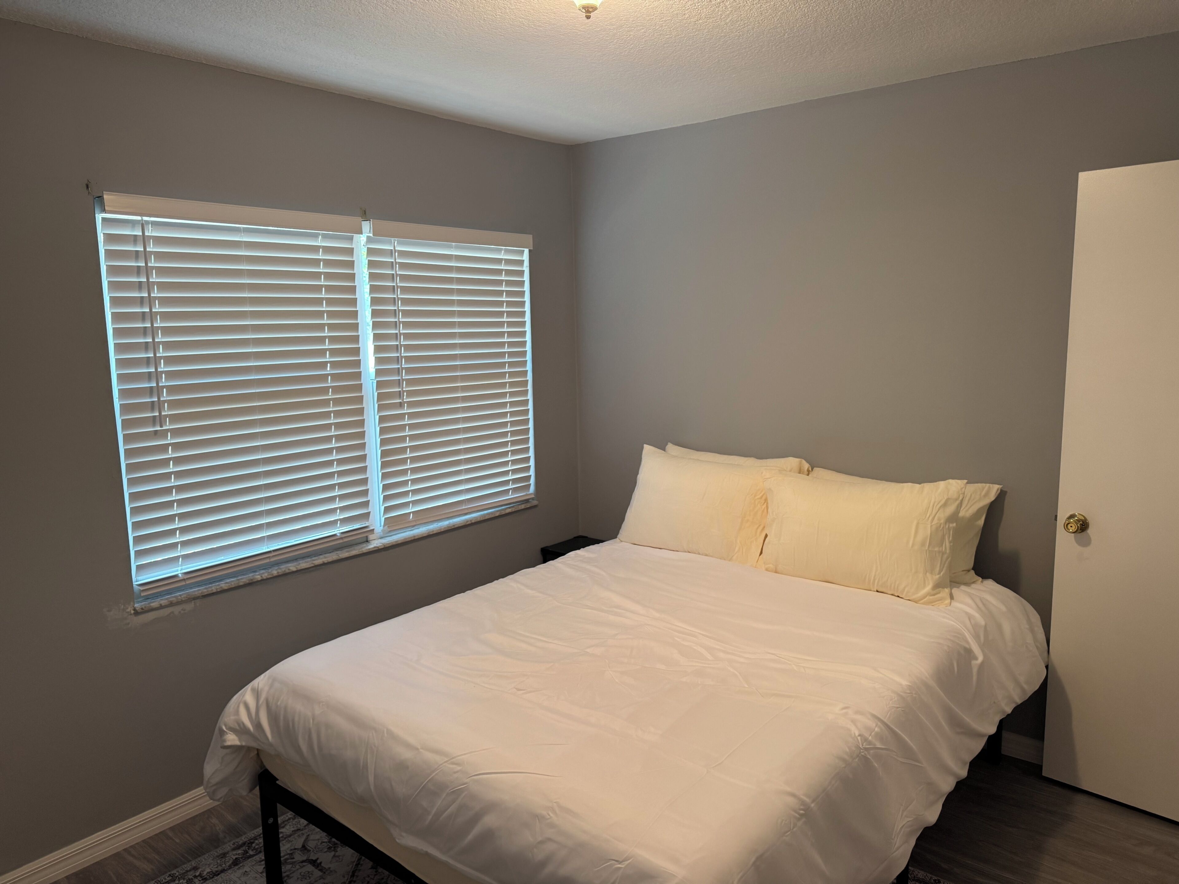A bedroom with a bed, a window with blinds, and a door.