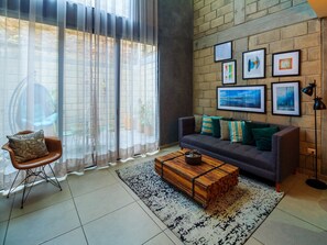 A living room with a sofa, a wooden coffee table, a chair, and a large window with sheer curtains. - Spacious Stylish Loft w Gym (Guadalajara)