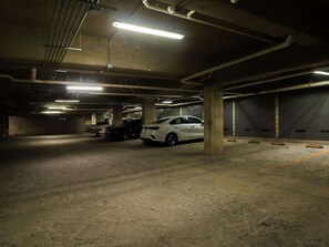 A parking garage with concrete pillars, fluorescent lighting, and a white car parked in the center. - Deluxe Single Apartment with Patio - 204 (Guadalajara)