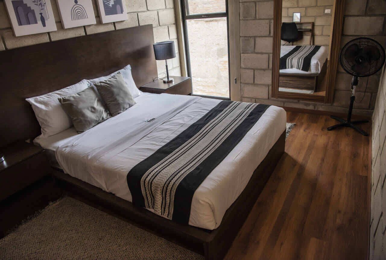 Une chambre à coucher avec un grand lit, une table de chevet, une commode, une lampe sur pied, un miroir et une fenêtre donnant sur un beau paysage.