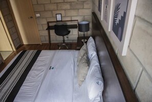 Une chambre à coucher avec un lit, un bureau, une chaise, une lampe et des tableaux encadrés accrochés au mur.