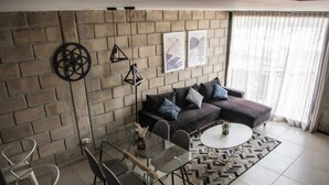 Ein modernes Wohnzimmer mit einem Ecksofa, einem Glastisch und einem gemusterten Teppich.