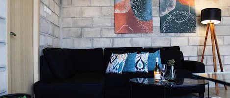 Un salon moderne avec un canapé noir, des œuvres d’art abstraites accrochées au mur, une lampe sur pied et une table basse en verre.