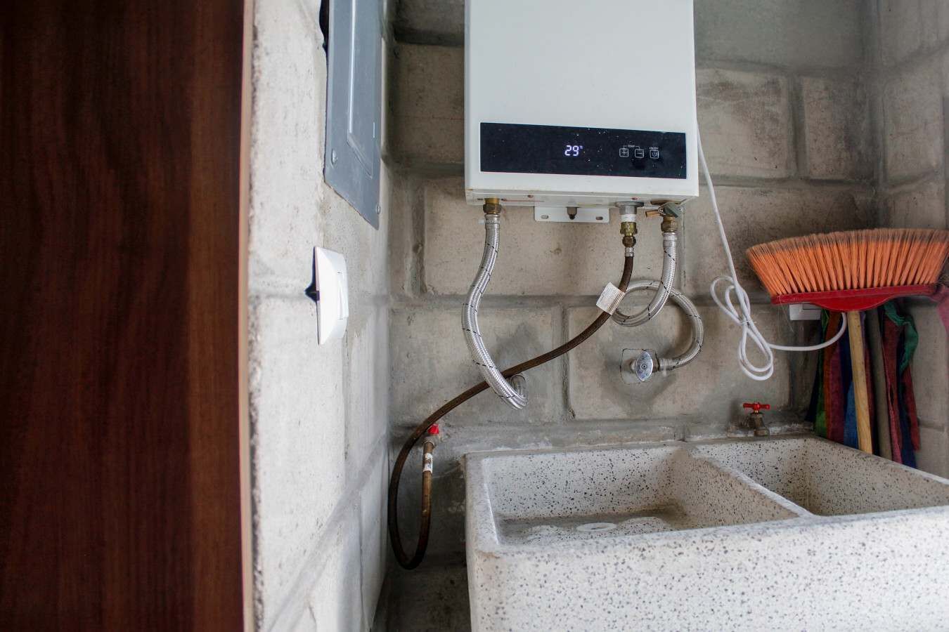 Un baño con un calentador de agua blanco, un lavabo y una escoba.