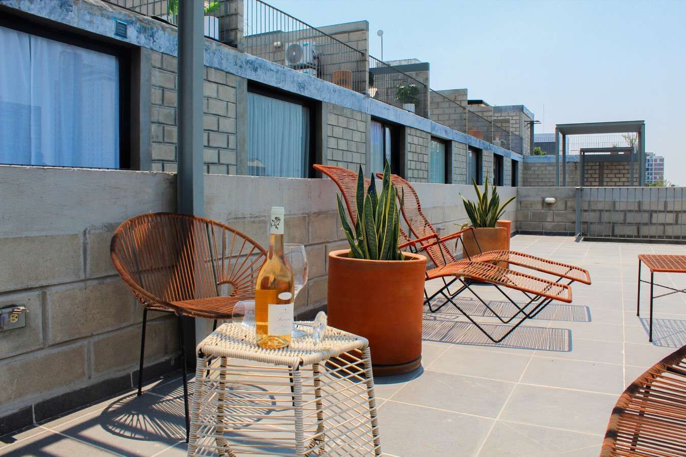 Une terrasse sur le toit, aménagée avec des meubles en osier, des plantes en pot et une bouteille de vin.