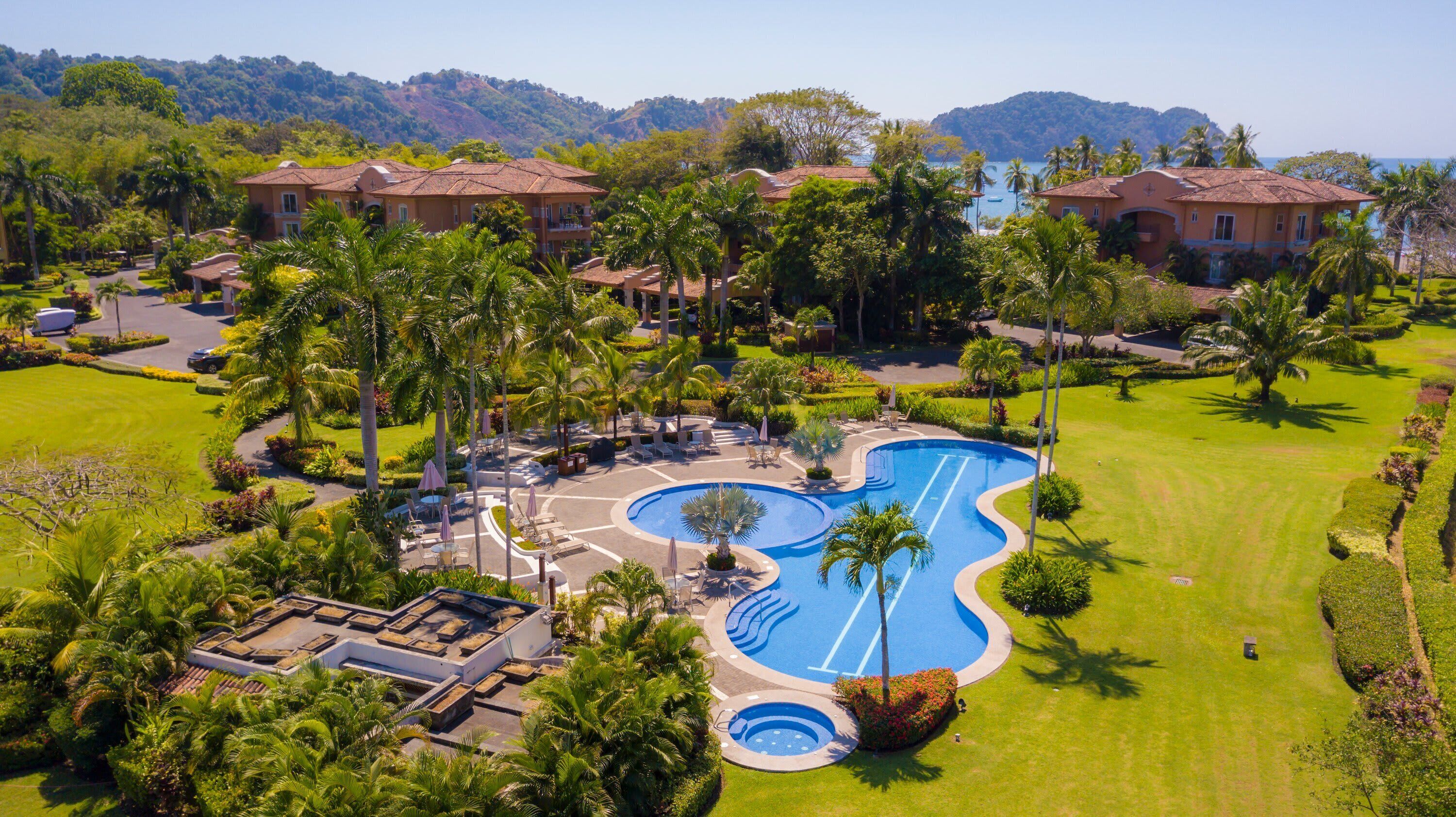 A resort with a swimming pool, palm trees, and a view of the sea.