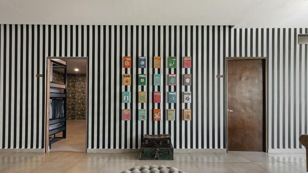 Ein Zimmer mit einer gestreiften Wand, einem runden Ottomanen und einem Koffer auf einem Teppich.