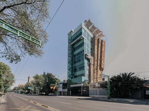 A modern building with a glass facade, a stone base, and a green metal structure on the left. - Low bed | Mixed Shared Room (Ciudad de México)
