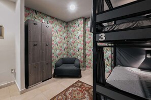 A bunk bed with a number '3' on the side, a grey sofa, a wardrobe with multiple compartments, and a floral wallpaper. - Low bed | Mixed Shared Room (Ciudad de México)