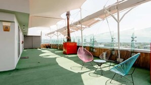 Eine Dachterrasse mit grüner Bodenfläche, einer roten Sitzgruppe und Blick auf Windkraftanlagen.