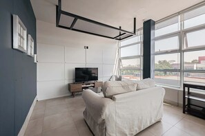 Ein modernes Wohnzimmer mit einer Couch, einem Flachbildfernseher und großen Fenstern mit Blick nach draußen.