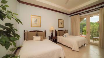 A hotel room with two beds, a ceiling fan, a balcony with curtains, and framed artwork on the walls.