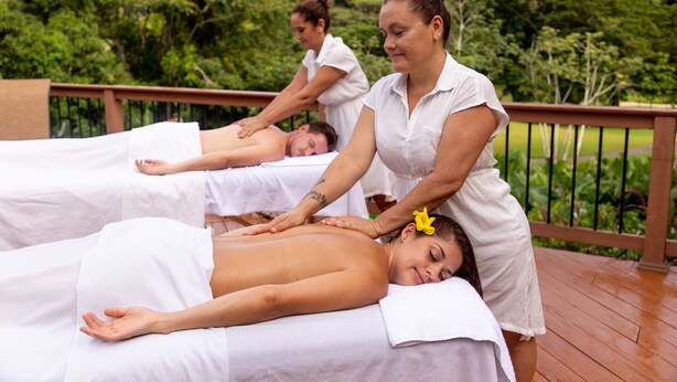Ein Spa-Bereich mit Massagetischen, einer Holzterrasse und Grünpflanzen im Hintergrund.