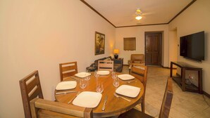 Ein Essbereich mit einem runden Tisch, gedeckt für vier Personen, einer Couch, einem Fernseher und einem Deckenventilator.