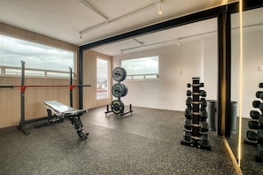 Ein Fitnessraum mit Gewichteinrichtungen, einer Hantelbank und großen Fenstern.